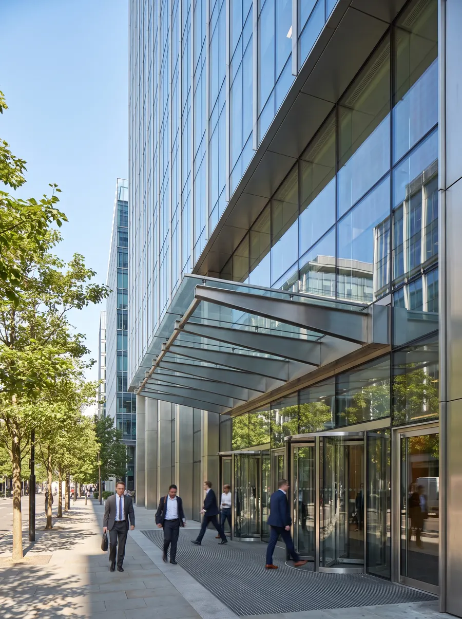Office workers walk into a glass office tower on a sunny morning